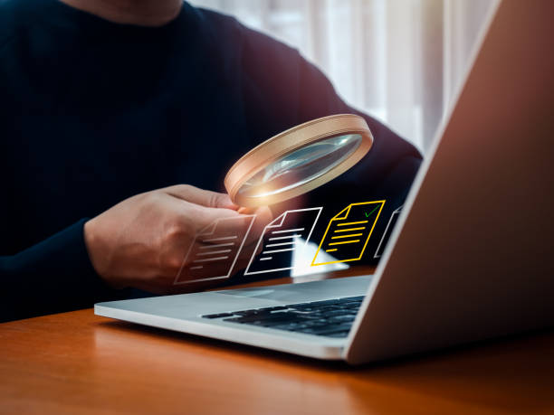 istock Electronic document check and data information searching online, files manager concept. Yellow documents file icon appear on magnifying glass in businessman hand while working with laptop computer. 2170903713