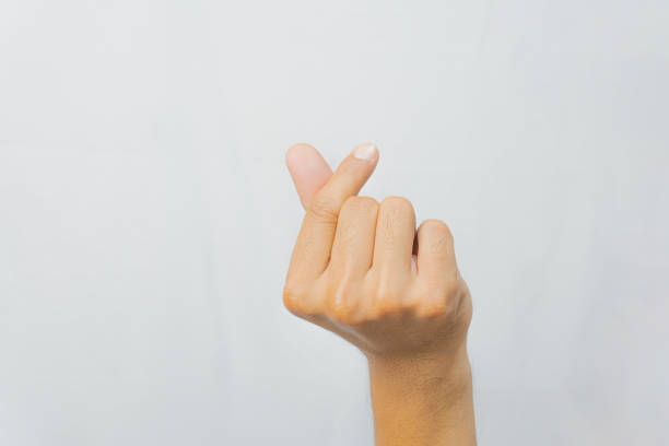 A young woman with long black hair is wearing a denim jacket and a beige turtleneck, smiling while pointing her right index finger upwards against a white background.