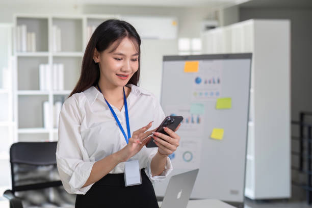 istock Young Accountant Using Smartphone in Modern Office Setting with Charts and Laptop in Background 2170906549