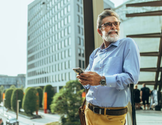istock Handsome senior businessman standing at street and using smart phone for communication. Modern buildings in background. 2170906904