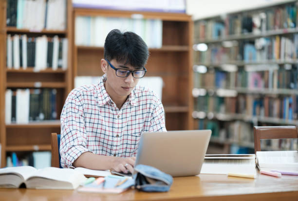 istock Young Asian male sitting inside a library alone doing research. Man working on a project. Young man doing research for a case. 2170911196
