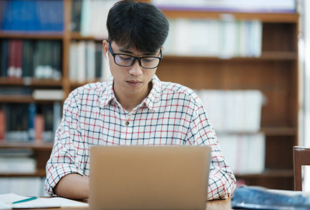 istock Young Asian male sitting inside a library alone doing research. Man working on a project. Young man doing research for a case. 2170911199