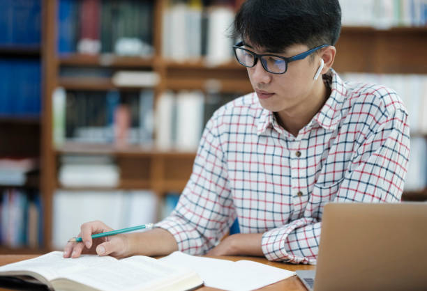 istock Young Asian male sitting inside a library alone doing research. Man working on a project. Young man doing research for a case. 2170911205