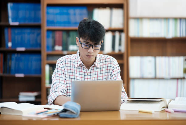 istock Young Asian male sitting inside a library alone doing research. Man working on a project. Young man doing research for a case. 2170911232