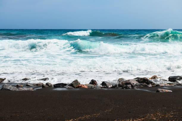 Santorini island, Greece. Waves on the beach. Perissa beach with black volcanic sand. Blue sea and the blue sky.