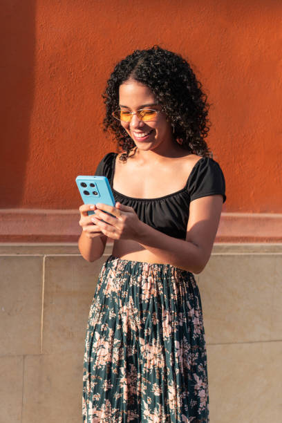 istock Smiling woman using smartphone outdoors against an orange wall. 2170928943