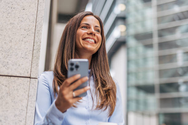 istock A young, cheerful businesswoman, smiling while holding coffee  and using her smartphone on the city street, with modern buildings in the background. 2170929855