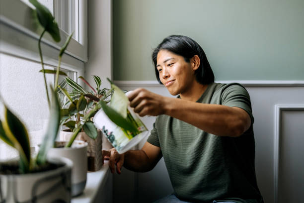 Young casually clothed man watering flowers at home
