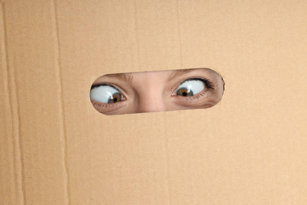Hole in cardboard with young woman eyes