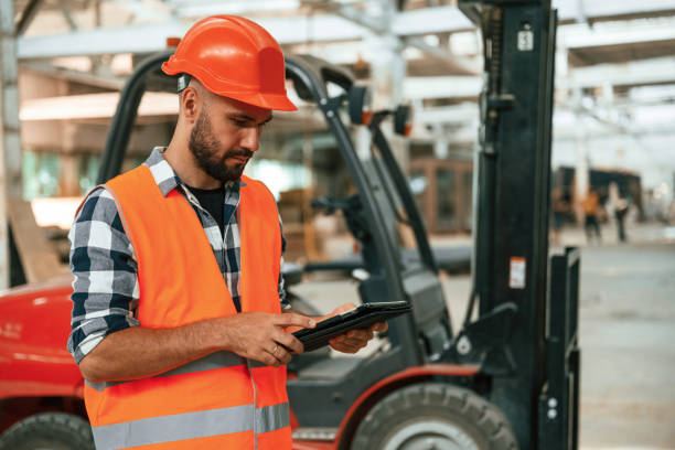 istock Forklift is behind, digital tablet in hands. Industrial worker in wooden warehouse 2170937582