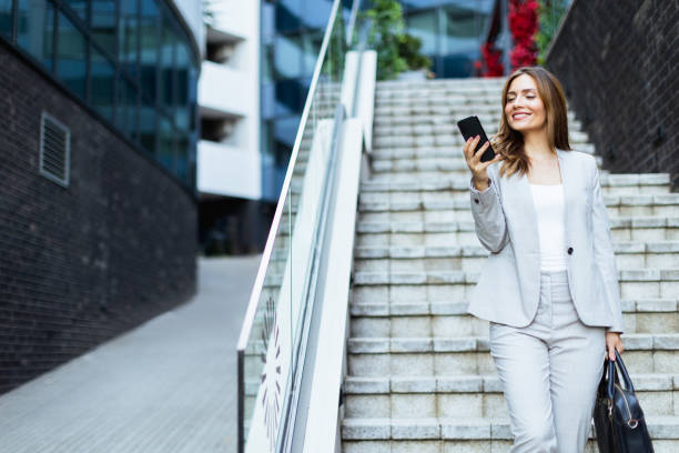 istock Professional woman smiles while checking her smartphone as she walks down sleek urban steps during a sunny afternoon in the city 2170942894