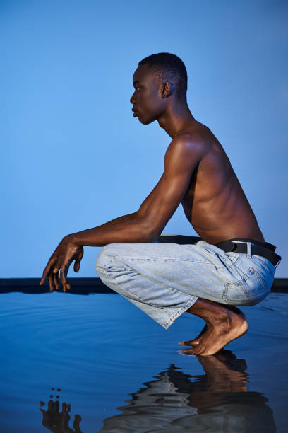 istock A young man crouches thoughtfully by a reflective surface in an artistic setting 2170953820