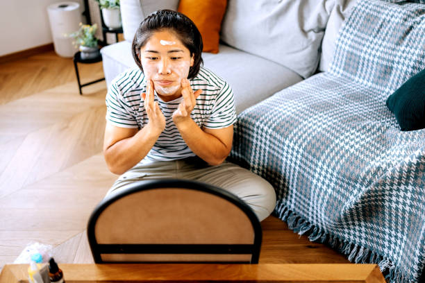 istock Young casually clothed man doing skincare routine, applying face cream on his face while sitting on a floor at home 2170954059