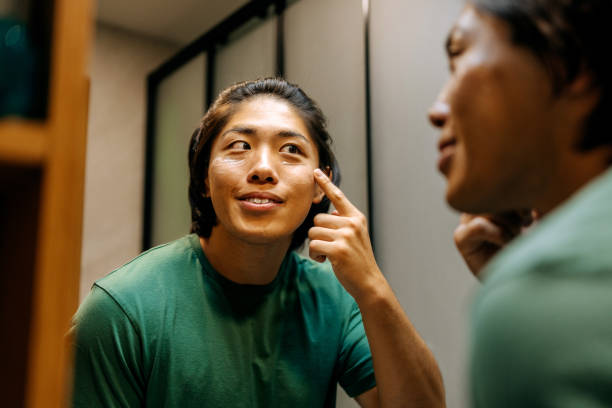 istock Young smiling man applying face cream under eyes while looking himself at the mirror at home 2170954128