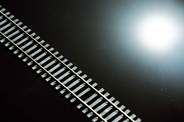 Toy railway and sun on glossy black background. Railway line. Selective focus effect. Rails and sleepers on dark background.