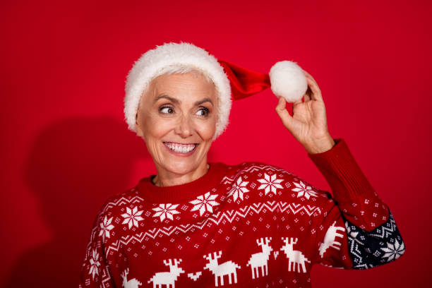 istock Photo portrait of attractive senior lady look empty space excited touch pompom dressed theme party sweater isolated on red color background 2170959310