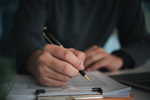 istock Close-up of a hand holding a pen writing on a document attached to a clipboard, document review signing and paperwork management. legal processes. 2170961625