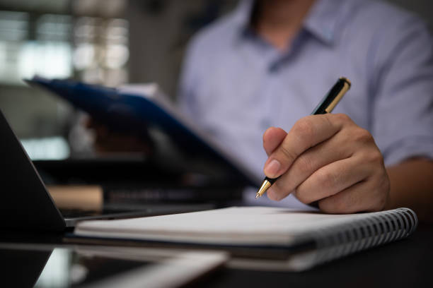 istock Business professional taking notes in a notebook while reviewing documents at a desk planning organization and business strategy development. Represents business analysis. 2170961633