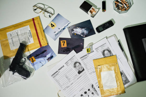 Investigating Crime Scene Evidence on Office Desk Setup Collection of crime scene evidence on an office desk includes photographs, cigarette butts, glasses, handgun, and criminal profiles laid out systematically evidence-bag-forensic-science-bag-label stock pictures, royalty-free photos & images