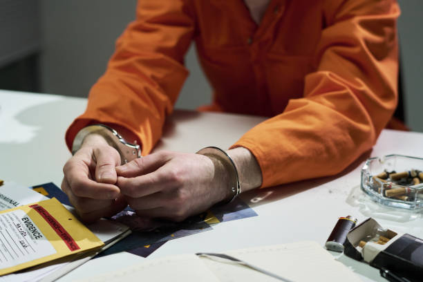 istock Handcuffed Person Wearing Orange Uniform Sitting at Desk 2170970755