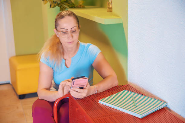 Woman in activewear using a smartphone while sitting at a desk with a striped book of exercises, blending technology and organization.