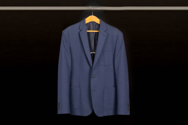 Front view of a classic blue blazer hanging neatly on a wooden hanger against a dark background.