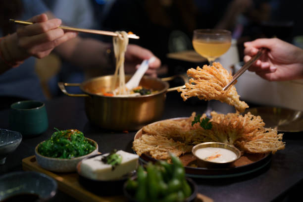 A close-up view of people enjoying a vegetarian dinner, featuring crispy deep-fried enoki mushrooms and a bowl of ramen noodles in a cozy vegetarian restaurant.
