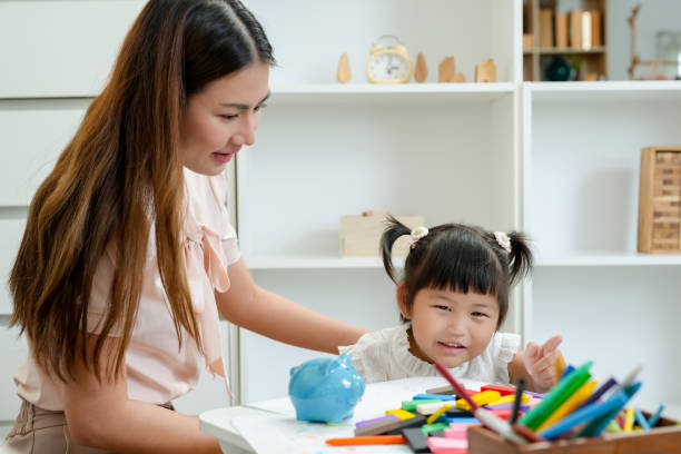 istock Asian woman sitting with toddler who is smiling while engaged in creative activity using colorful pencils and blocks. Scene reflects positive interaction and development in a comfortable home setting. 2171002378