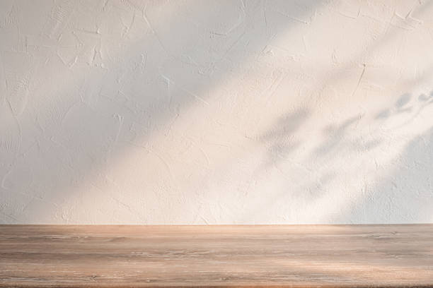 istock Bright, minimalist wooden table by textured light wall with soft shadows in cozy, well-lit interior space 2171002409
