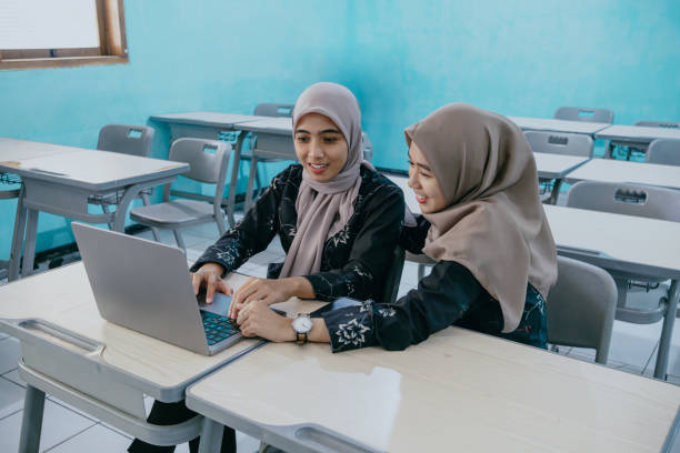 Cheerful Asian Muslim women friend working using laptop computer. Young Asian Muslim female colleague discussing planning projects and exchanging ideas in classroom.