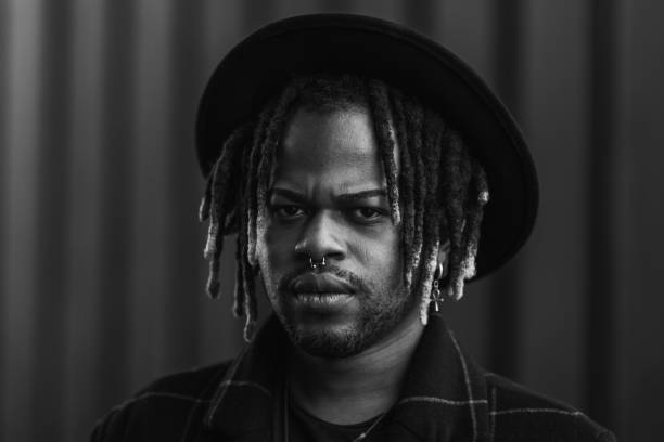 Informal bearded ethnic man with dreadlocks and in hat looking at camera standing on street