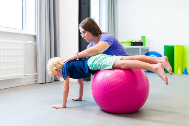 istock Young boy with female physical therapist exercising using ball during therapy session. Child physical therapy. Bilateral coordination. 2171012244