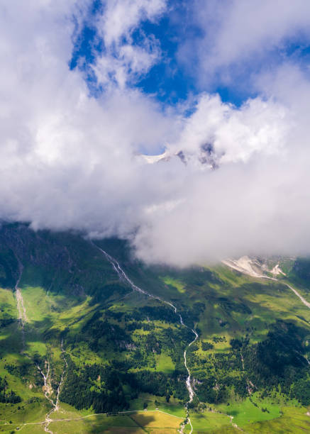 Majestic high alpine mountains covered with green vegetation under a bright blue summer sky. Streams of water flowing down the mountains. Grossglockner. Hohe Tauern National Park, Austria