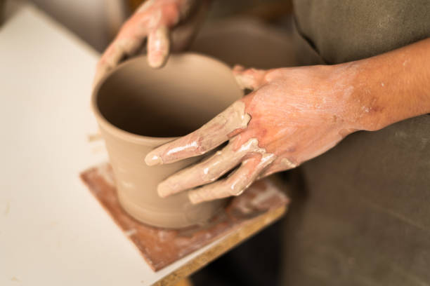 istock Potter's hands gently placing a newly crafted clay vase on a square tile to dry 2171032285