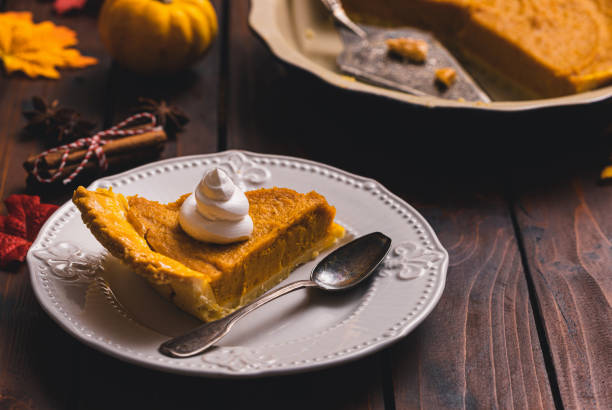 Slice of Thanksgiving holiday pumpkin pie with whipped topping served on a plate