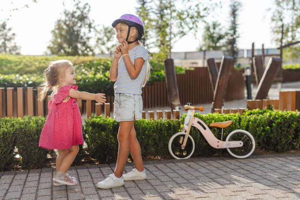 Photo of a cute little blonde hair girl wearing a protective bicycle helmet and talking with her sister
