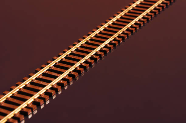 Toy railway on glossy red background. Railway line. Selective focus effect. Rails and sleepers on dark background.