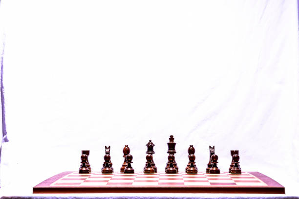A wooden chess board with a white background. The board is full of pieces, including a king, queen, rooks, knights, bishops, and pawns. Concept of strategy and competition