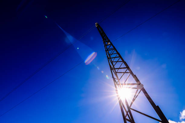 A tall power pole with a bright sun shining on it. The sky is clear and blue. The sun is shining brightly on the pole, creating a beautiful and serene scene