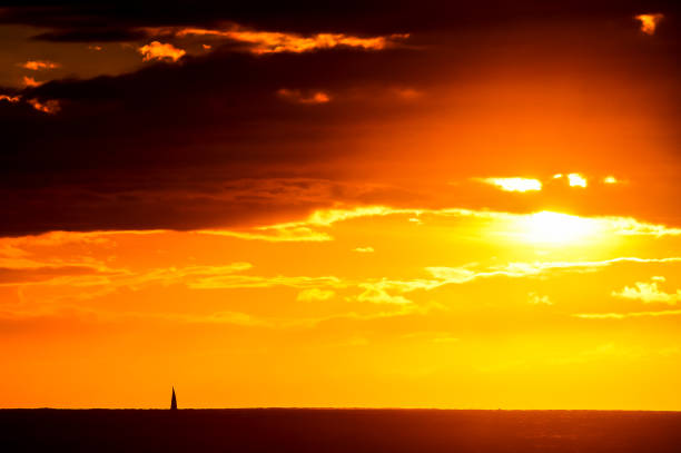 A beautiful sunset with a boat in the foreground. The sky is filled with clouds and the sun is setting