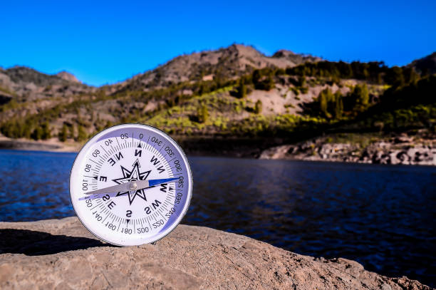 A compass is sitting on a rock by a body of water. Concept of adventure and exploration, as the compass is a tool used for navigation and finding direction. The presence of the water adds a serene