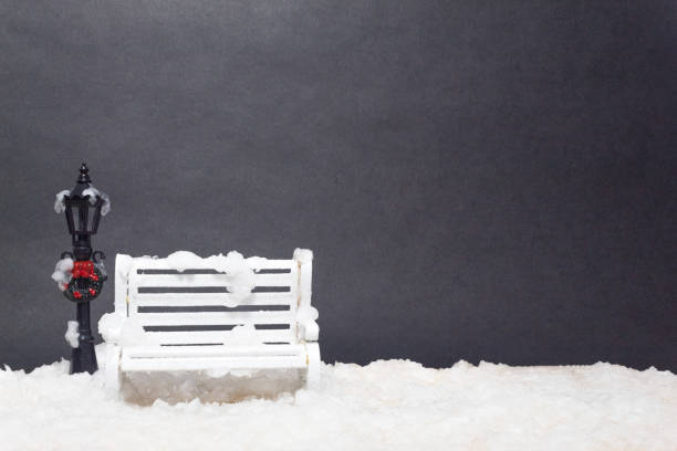 A lamp post decorated with a Christmas wreath next to a white park bench with snow around it. Miniature model with copy space.
