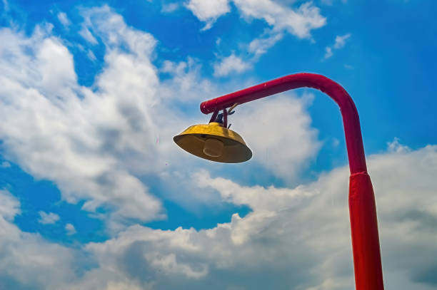 Red street lamp with yellow underside against blue sky and white clouds, unique low angle view, vibrant colors.