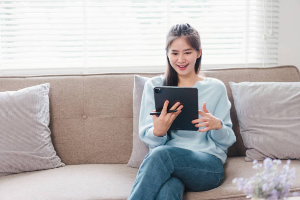 istock Smiling Asian Woman Relaxing on Couch While Using Tablet at Home. 2171059205