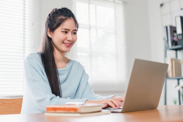 istock Smiling Asian woman typing on laptop while sitting at home, focused on work or study in a comfortable setting. 2171059215