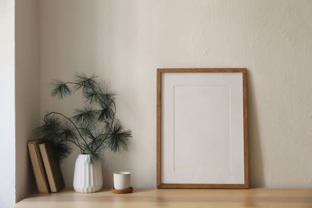 istock Christmas breakfast still life. Minimal winter artistic composition. Blank vertical thin wooden picture frame mockup, cup of coffee on cork tray, table. Pine tree branches modern white vase, old books 2171059572