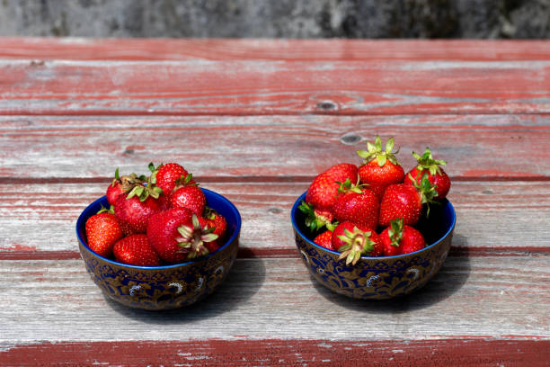 Strawberry in the two blue bowls on rustic table in garden. Ripe strawberries on table.