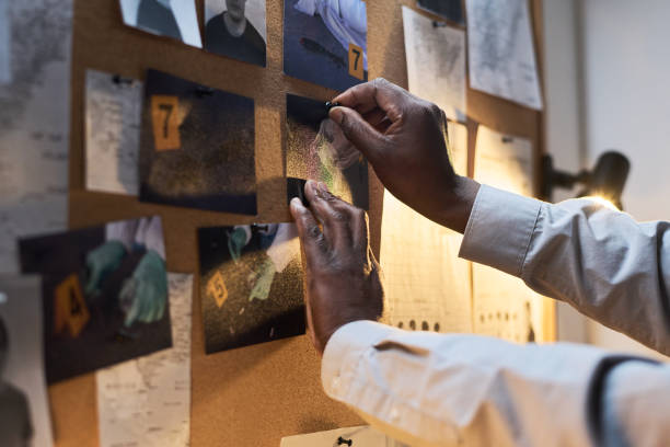 Investigating Crime Scene Evidence on Bulletin Board Hands pinning photos and notes on bulletin board in dimly lit room, with various pieces of evidence related to crime scene under investigation spy games stock pictures, royalty-free photos & images