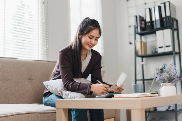 istock A young woman is sitting on cozy sofa, smiling as she writes on notepad, surrounded by bright and inviting living space. atmosphere is warm and productive, perfect for creativity. 2171060057
