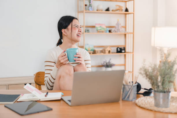 istock A woman sitting at desk, holding blue mug, smiling joyfully while working on laptop. cozy workspace features plants and decorative items, creating warm atmosphere. 2171060266